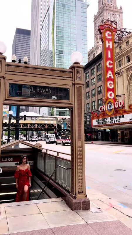 Roopsi Bansal in a red sequin off-shoulder dress, emerging from a subway station entrance beneath the Chicago Theatre marquee