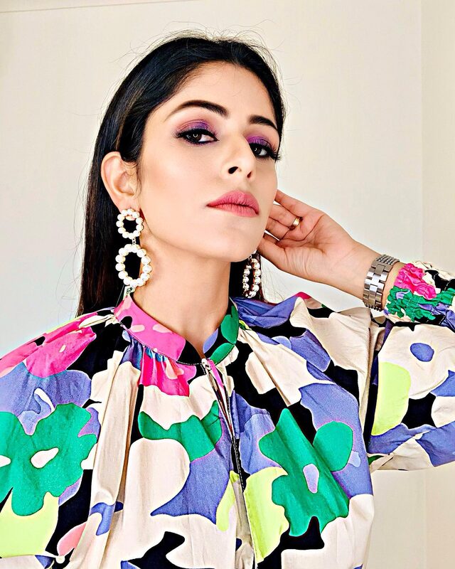 A close-up portrait wearing a bright tropical floral blouse, purple smokey eye, and pearl drop earrings