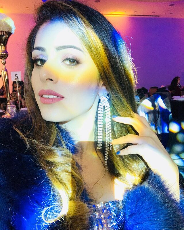 Close-up glam makeup look with soft eyeshadow and fringe drop earrings, wearing a blue faux-fur wrap under colorful event lighting