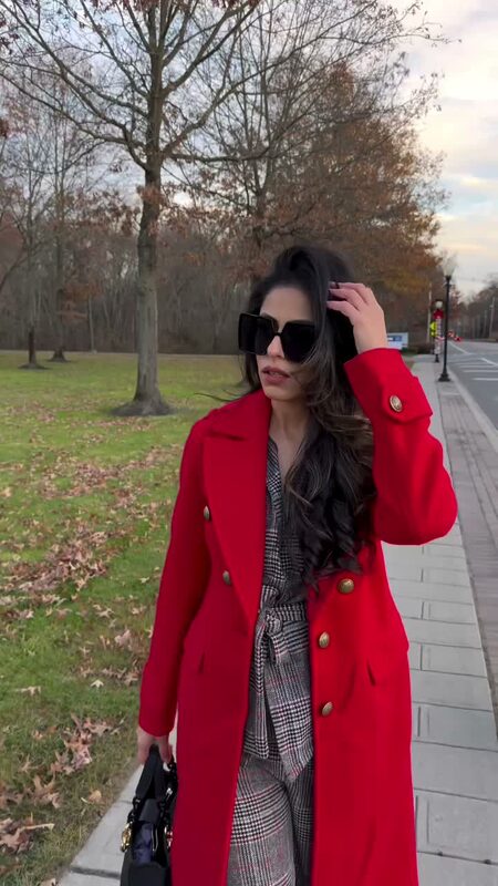 Roopsi Bansal in a red double-breasted coat from Express and oversized sunglasses walking along a park path in late fall