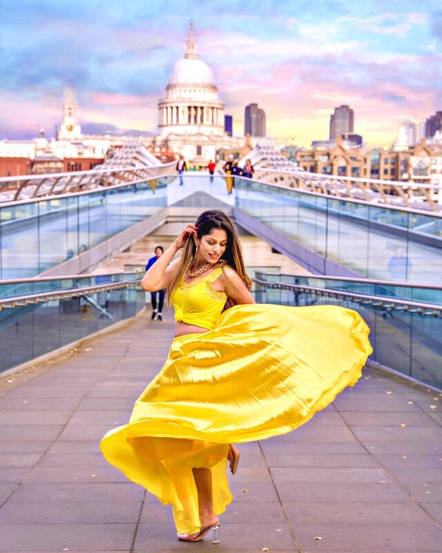Roopsi Bansal twirling in a bright yellow crop top and full satin skirt on the Millennium Bridge, with St. Paul's Cathedral in the background at sunset